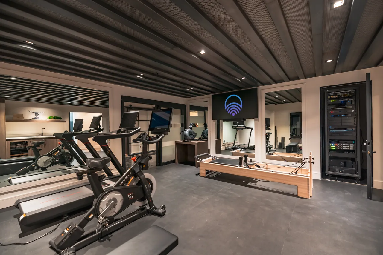 Home training room with connected equipment and the AV rack visible behind glass