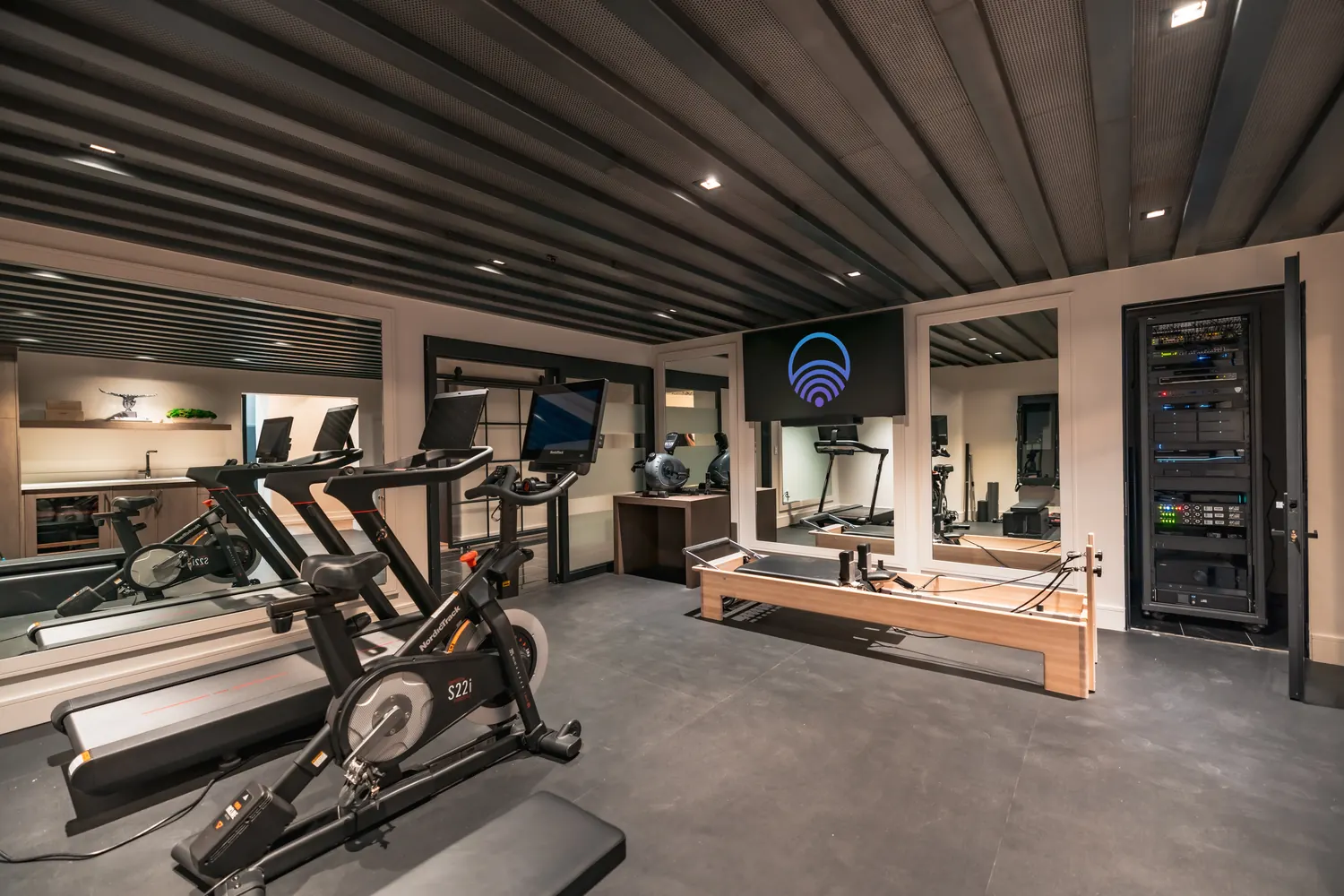 Home gym with connected equipment and the AV rack visible behind glass