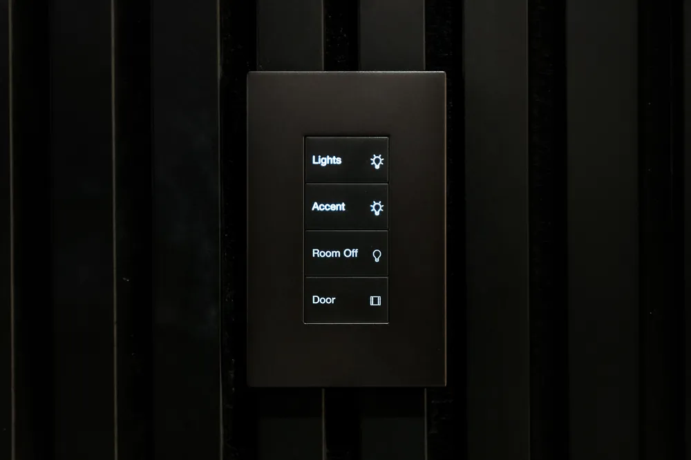Engraved four-button lighting keypad mounted on a black slat wall