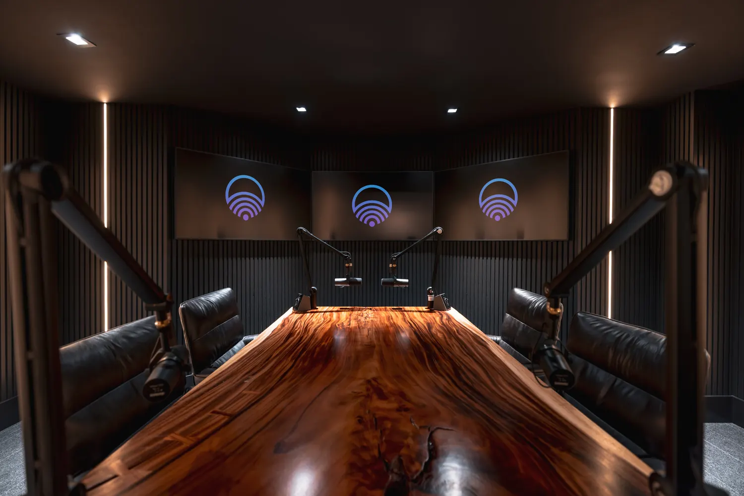 Podcast studio with slat-wall acoustics, live-edge table and three displays